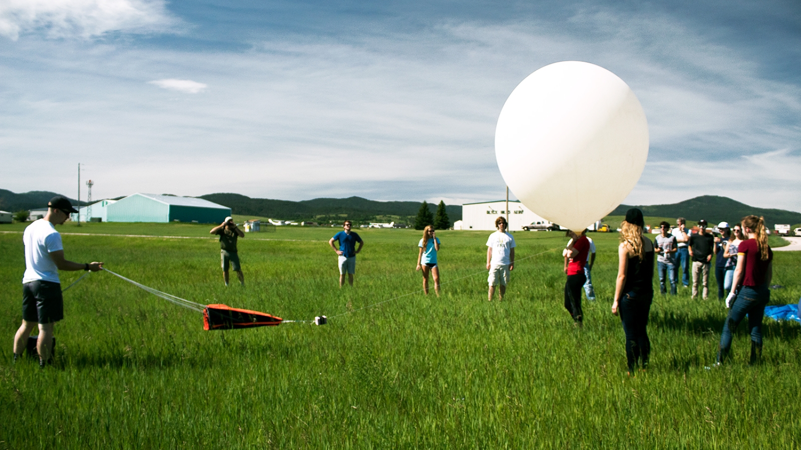 A crowd watches a balloon launch in a field